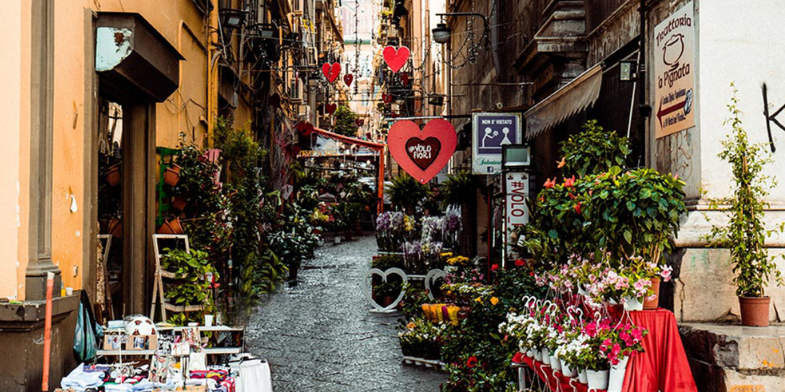 Une ruelle étroite et colorée avec des cœurs rouges suspendus.
