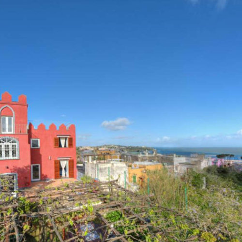 Bâtiment rouge et vignoble avec vue panoramique sur la mer.