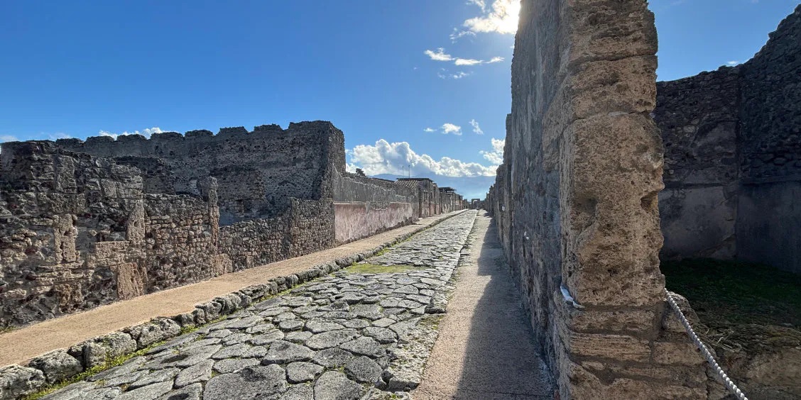 Rue antique pavée de Pompéi avec ruines romaines et murs en pierre.