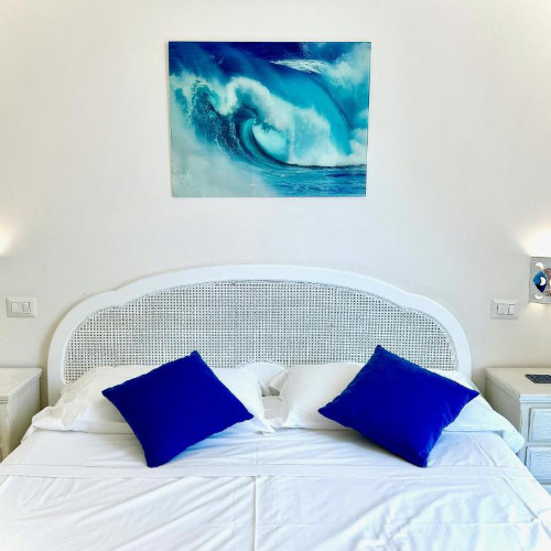 Intérieur d'une chambre décorée sur le thème de la mer, avec une tête de lit en rotin blanc, des coussins bleu vif et un tableau de vague.