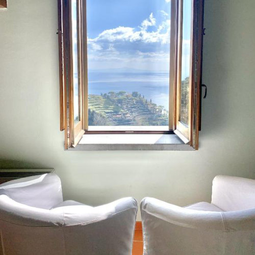 Vue de fauteuils blancs vers une fenêtre ouverte sur un panorama côtier.