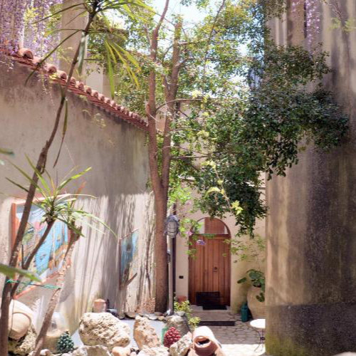 Cour intérieure ensoleillée avec murs en pierre et végétation abondante.