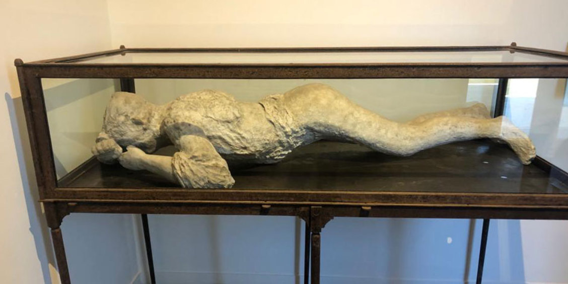 Moulage réaliste d'une victime de Pompéi dans sa vitrine de musée.