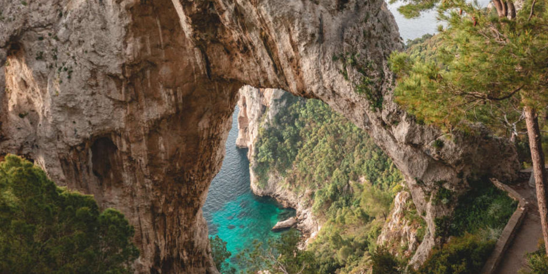 Vue plongeante à travers l'Arco Naturale de Capri sur une mer turquoise et une côte rocheuse sauvage.