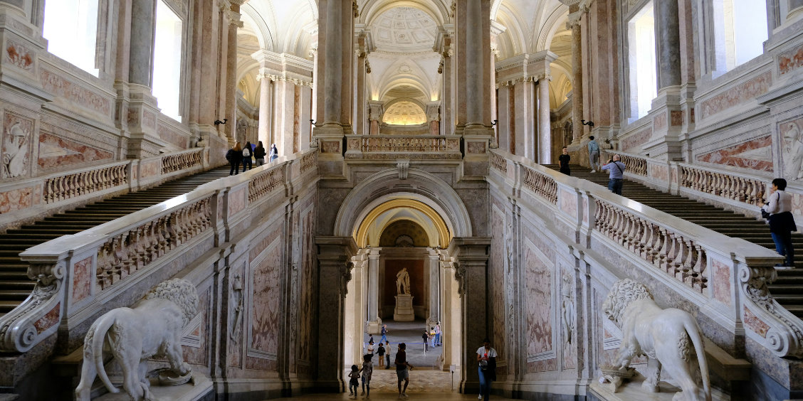 Grand escalier d’honneur du Palais royal de Caserte avec marbres, statues de lions et voûtes monumentales.