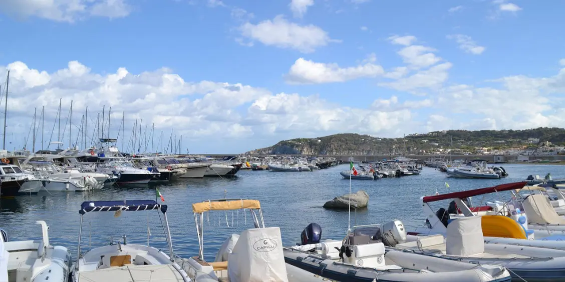 Vue du port d'Ischia rempli de bateaux sous un ciel bleu parsemé de nuages.