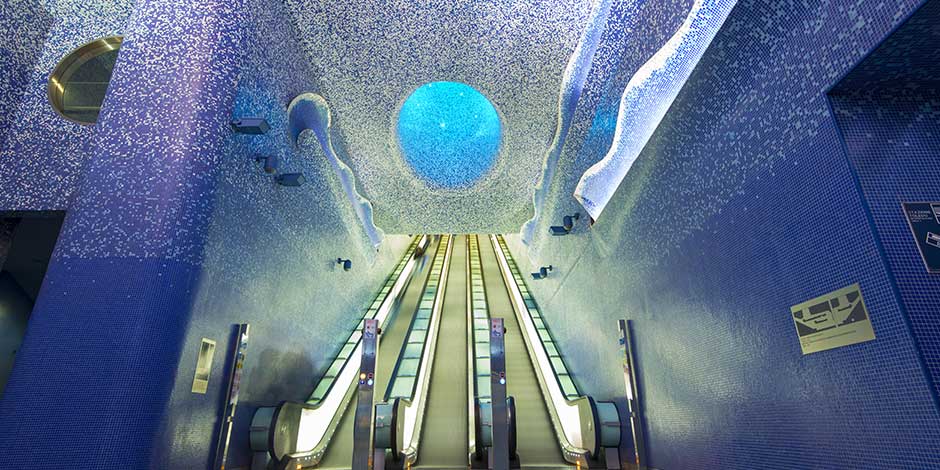 L'intérieur spectaculaire de la station de métro Toledo à Naples, orné de mosaïques bleues et d'escaliers mécaniques montant vers la lumière.