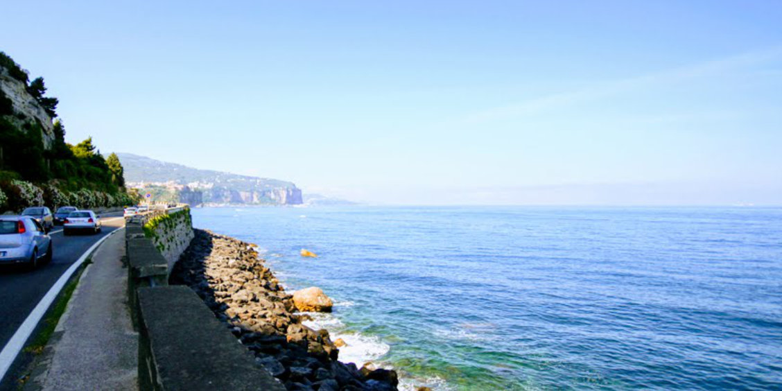 Route côtière vers Sorrente avec voitures, mer bleue et falaises au loin.