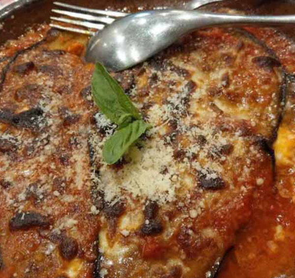 Aubergines à la parmigiana traditionnelles servies dans un plat en terre cuite avec sauce tomate, fromage fondu et basilic frais.
