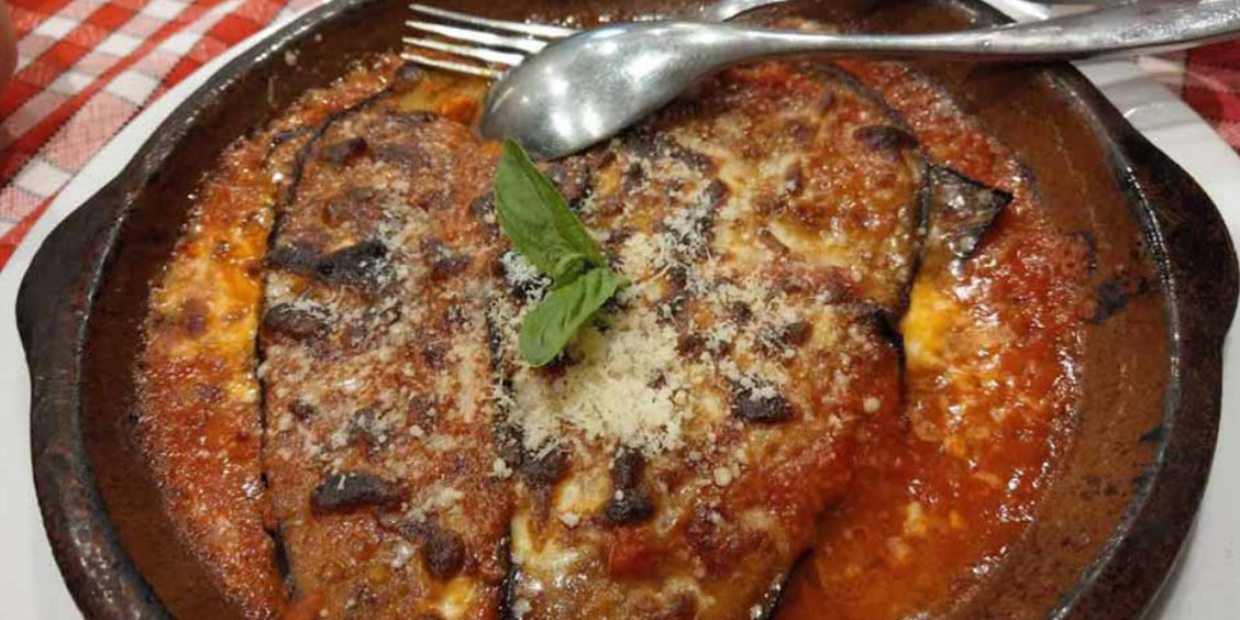 Aubergines à la parmigiana traditionnelles servies dans un plat en terre cuite avec sauce tomate, fromage fondu et basilic frais.