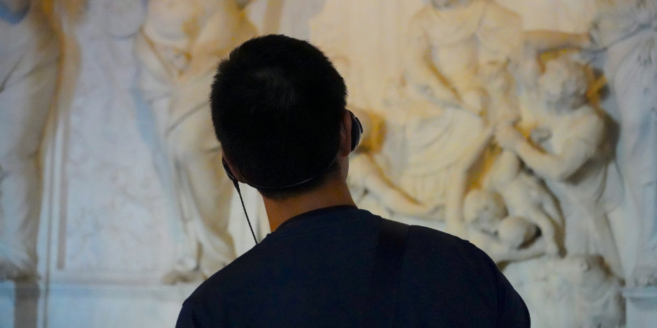 Visiteur utilisant un audioguide pour observer des sculptures antiques.