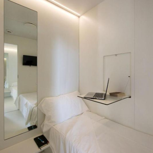 Chambre compacte et minimaliste dans un hôtel capsule à Naples avec lit et espace de travail.
