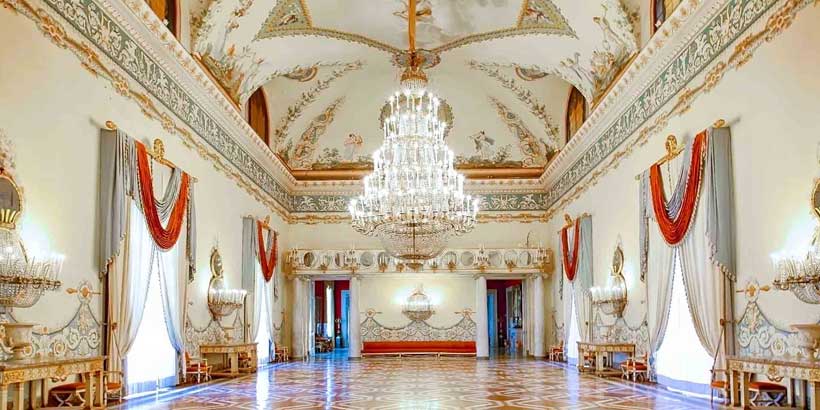 Somptueuse salle de bal du Musée de Capodimonte à Naples, caractérisée par un majestueux lustre central en cristal, des plafonds richement ornés de fresques et du mobilier doré.