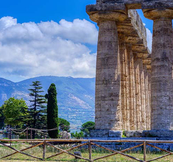 Temple antique de Paestum avec colonnes en pierre, montagnes et ciel bleu en arrière-plan.