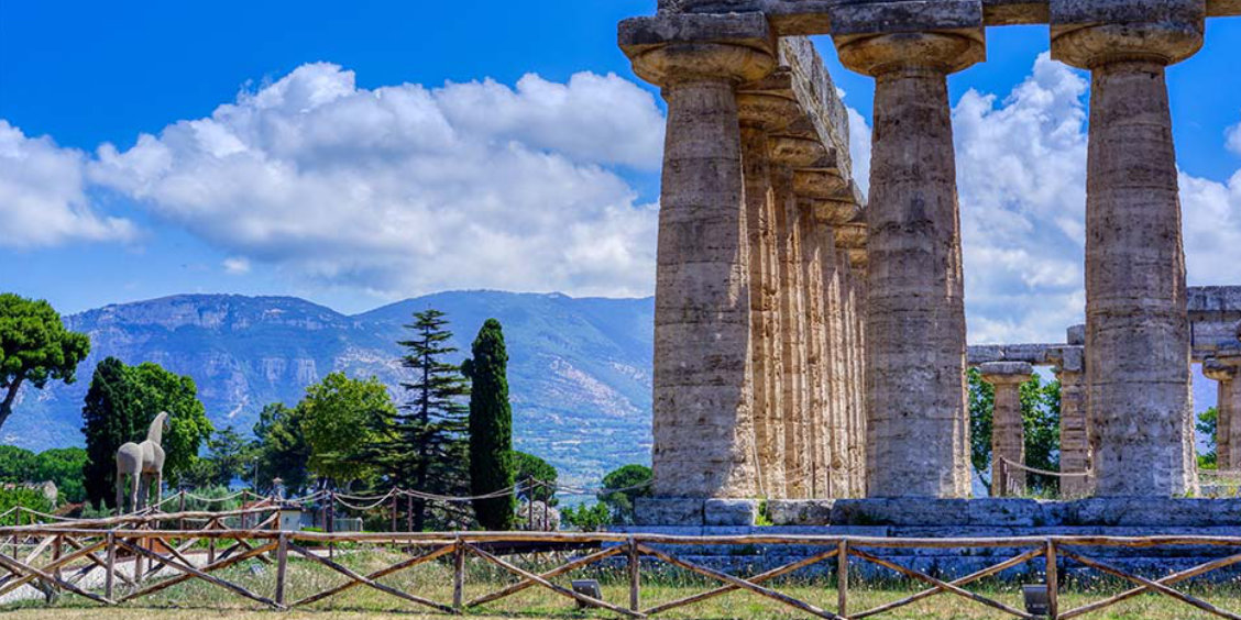 Temple antique de Paestum avec colonnes en pierre, montagnes et ciel bleu en arrière-plan.
