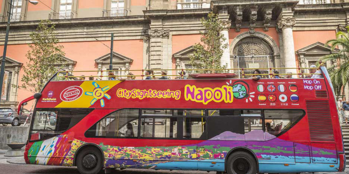 Bus touristique à arrêts multiples à Naples devant un bâtiment historique, idéal pour visiter la ville.