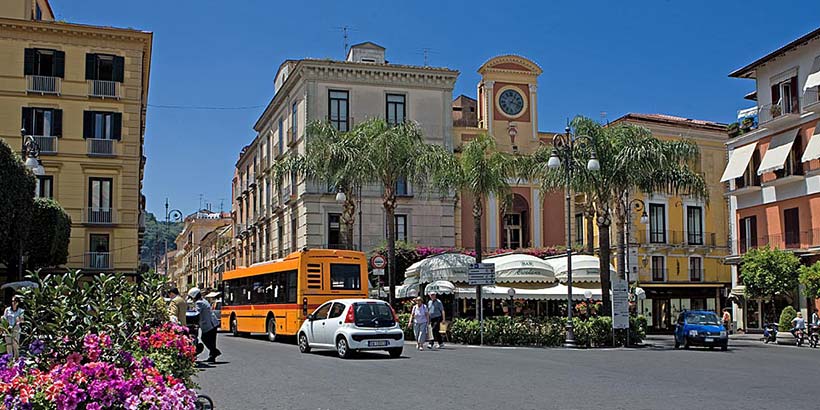 Bus à Sorrente sur la Piazza Tasso avec palmiers, voitures et bâtiments colorés.