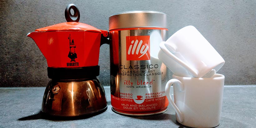 Cafetière italienne Moka rouge Bialetti à côté d'une boîte de café Illy et de trois tasses à expresso.
