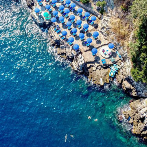 Plage rocheuse du Camping Santa Fortunata à Sorrente avec parasols bleus et eau turquoise.