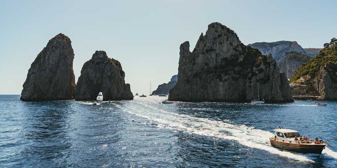 Bateau de passagers s'approchant des emblématiques rochers Faraglioni de Capri.