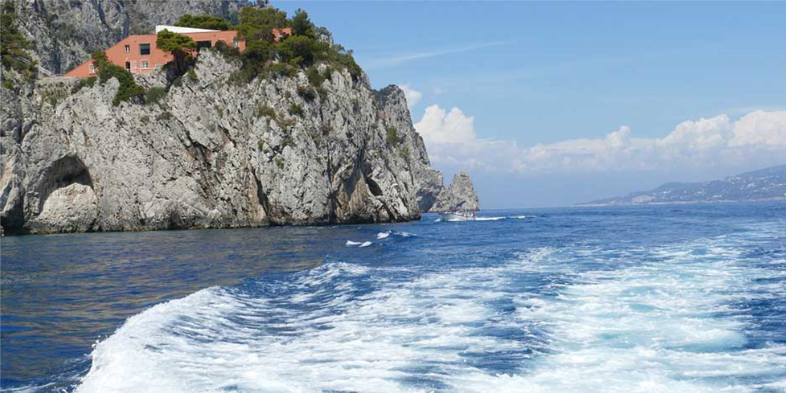 Sillage d'un bateau longeant les falaises de Capri avec la Villa Malaparte dominant la mer.