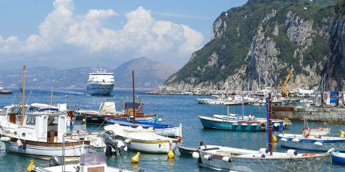 Le port de Marina Grande à Capri avec des barques et un ferry blanc arrivant au loin sous les falaises.