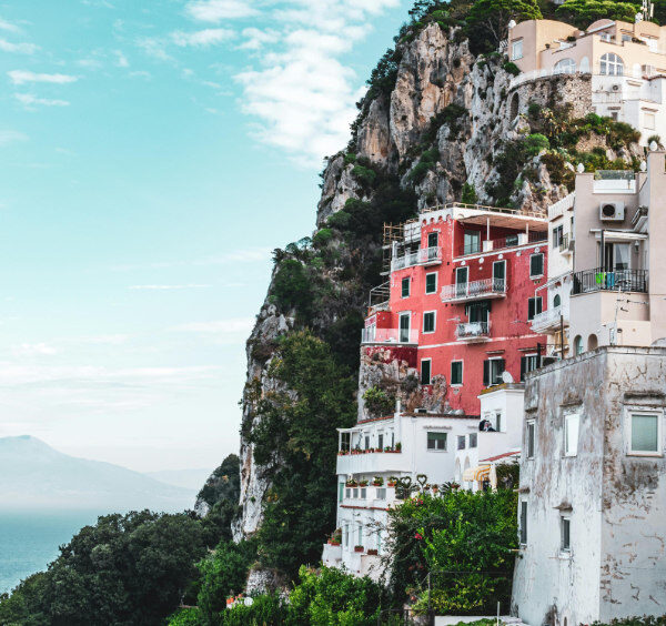Maisons colorées à flanc de falaise à Capri surplombant la mer avec la silhouette du mont Vésuve à l'horizon.