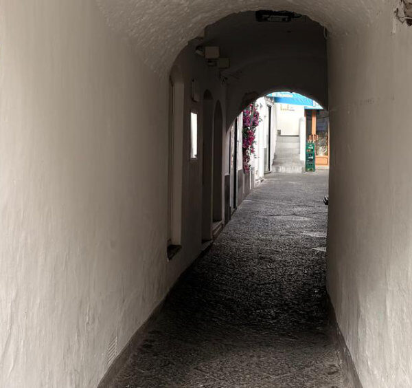 Passage voûté étroit à Capri avec des plaques indicatrices en céramique sur le mur gauche.