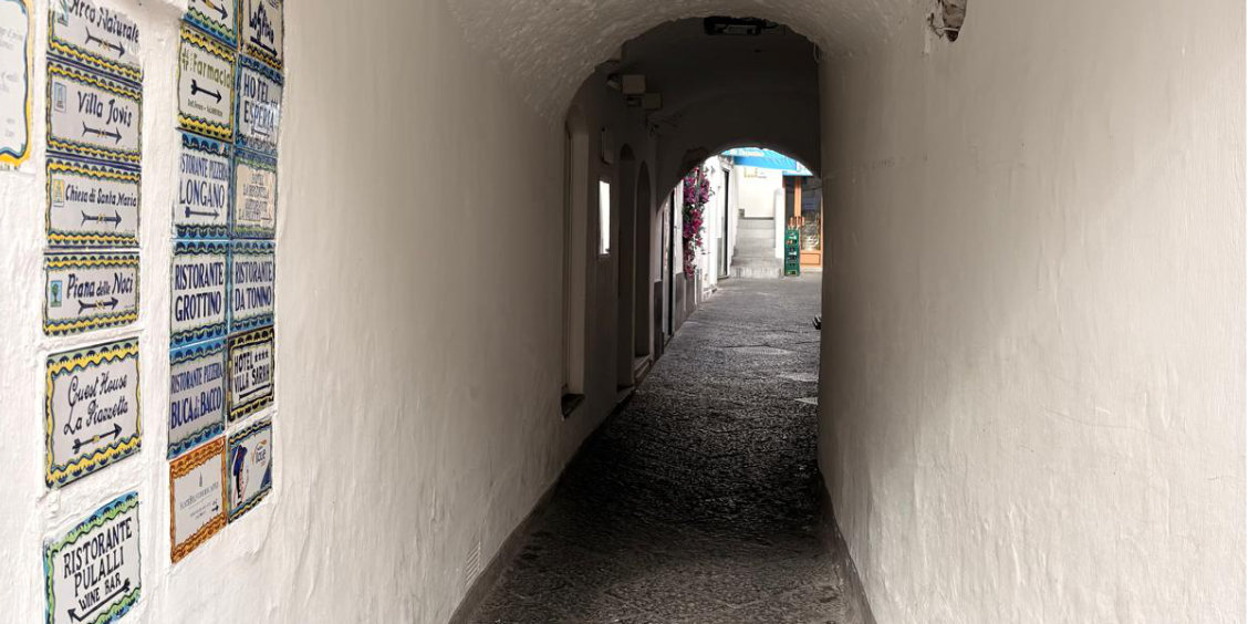 Passage voûté étroit à Capri avec des plaques indicatrices en céramique sur le mur gauche.