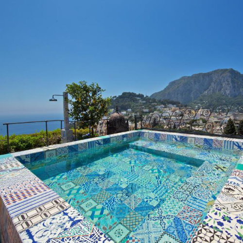 Petite piscine en mosaïque bleue de l'hôtel Capri Tiberio Palace avec vue panoramique sur Capri et les montagnes.