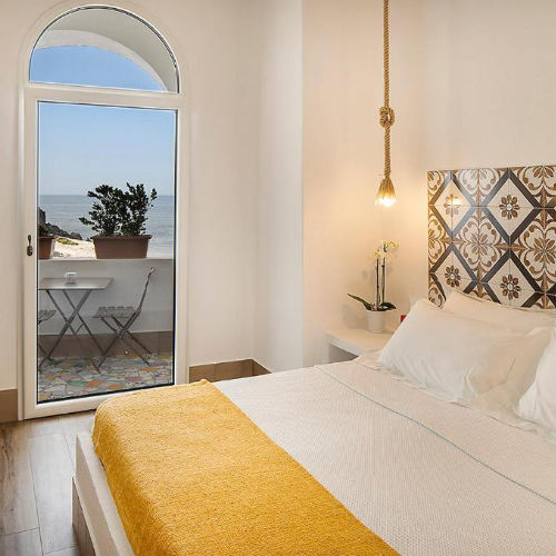 Chambre lumineuse avec tête de lit en faïence et balcon offrant une vue sur la mer.