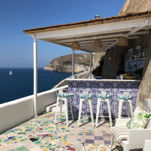 Bar extérieur au design méditerranéen avec tabourets blancs et vue panoramique sur la côte.