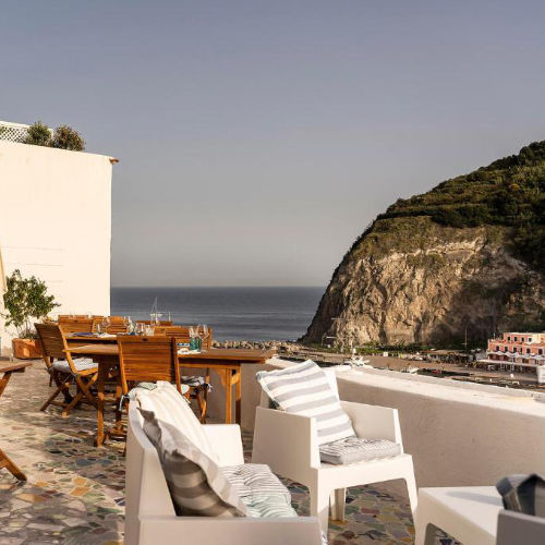 Terrasse de restaurant avec mobilier moderne et vue sur le promontoire de Sant'Angelo.