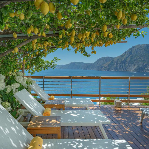 Terrasse avec transats sous citronniers et vue sur la mer, hôtel avec panorama sur la côte amalfitaine.