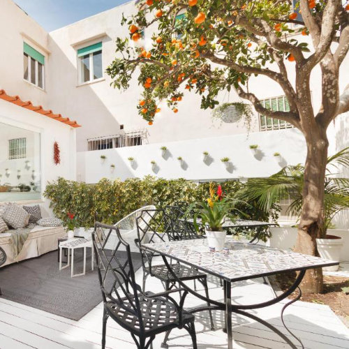 Patio fleuri à Capri avec table en mosaïque, chaises en fer forgé et grand oranger chargé de fruits.