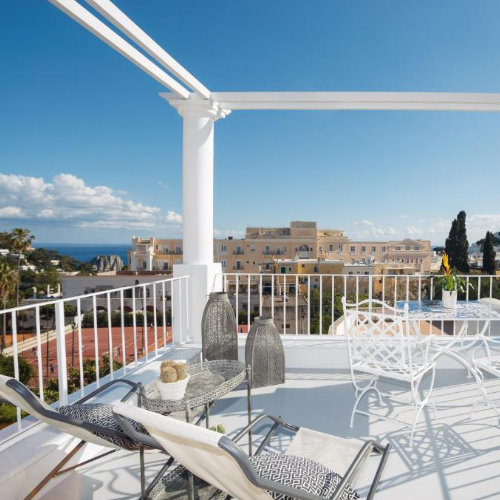 Toit-terrasse de la Casa di Capri avec mobilier blanc, transats et vue panoramique sur la ville et la mer.
