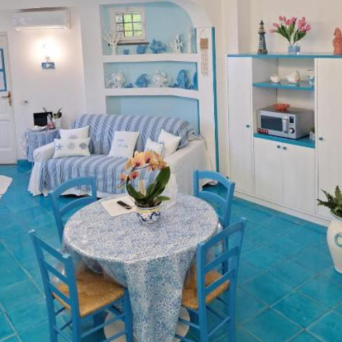 Salon lumineux à Sorrente avec canapé, table ronde et décoration bleue de style méditerranéen.