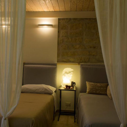 Chambre élégante avec lits à baldaquin, voiles blancs et lampes originales en forme de bustes classiques.