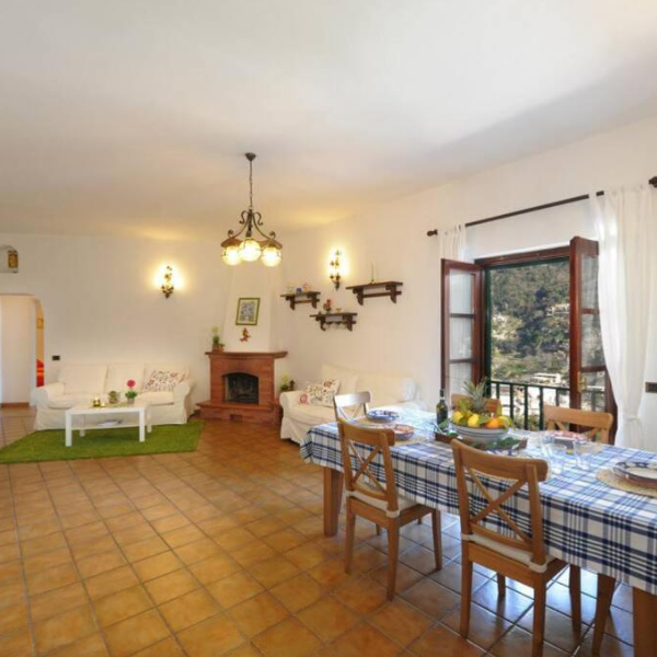 Salon de Casa Siria à Positano avec table à manger, cheminée et vue sur la côte.