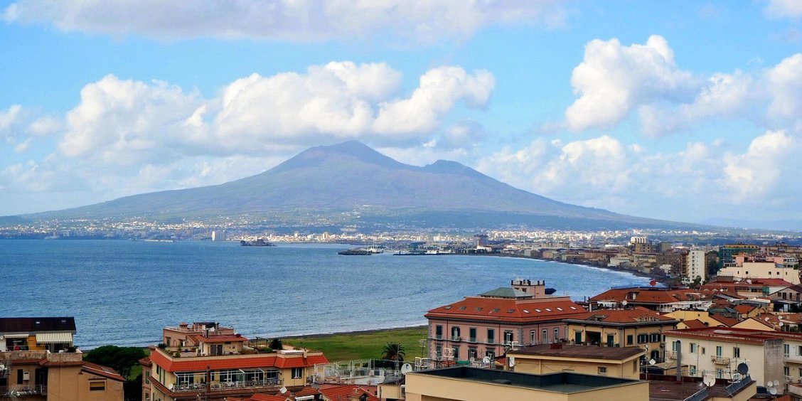 Vue panoramique sur la ville de Castellammare di Stabia et la mer avec le mont Vésuve en arrière-plan sous un ciel nuageux.