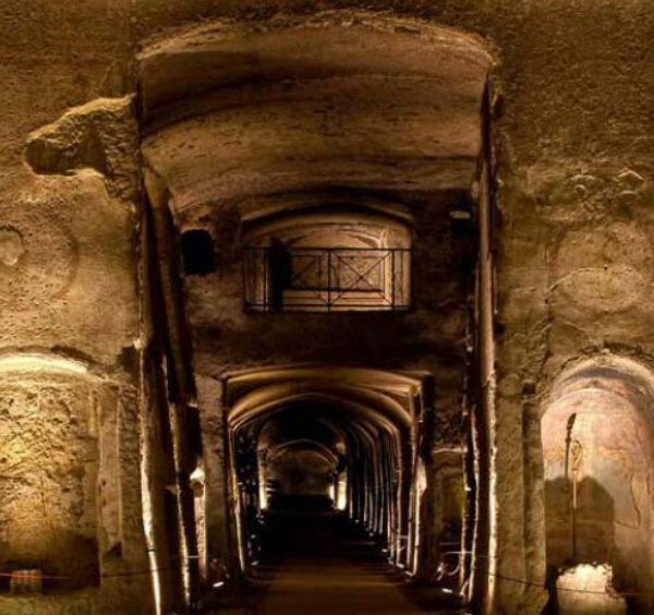 Intérieur des catacombes de San Gennaro à Naples, avec galeries souterraines voûtées, niches funéraires et éclairage tamisé.