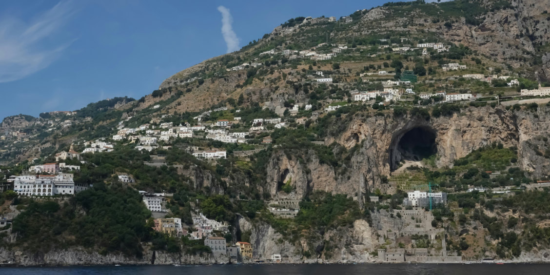 Maisons blanches accrochées aux falaises de Conca dei Marini avec une grotte naturelle.