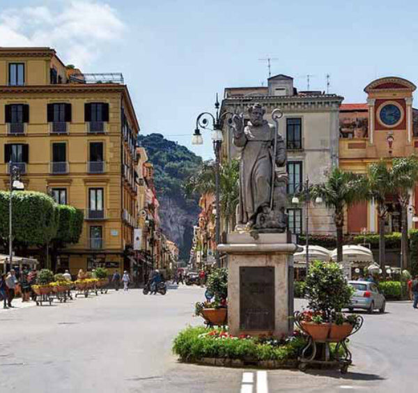 Piazza Tasso à Sorrente avec statue centrale, cafés, bâtiments colorés et petit train touristique.