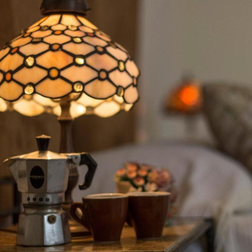 Détail d'une table de chevet au Cerasiello avec une lampe de style Tiffany allumée, une cafetière Moka traditionnelle et deux tasses à expresso.