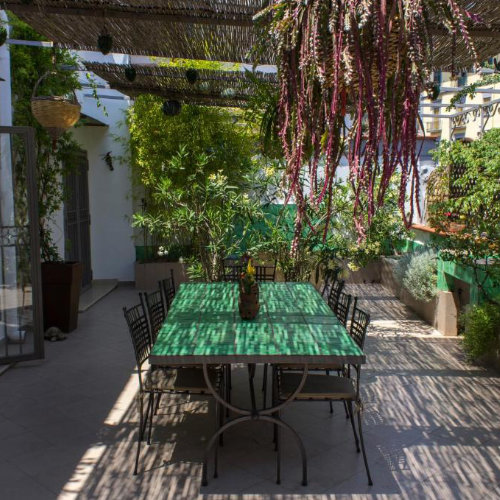 Terrasse extérieure spacieuse et fleurie avec une grande table en carreaux verts sous une pergola en bambou.