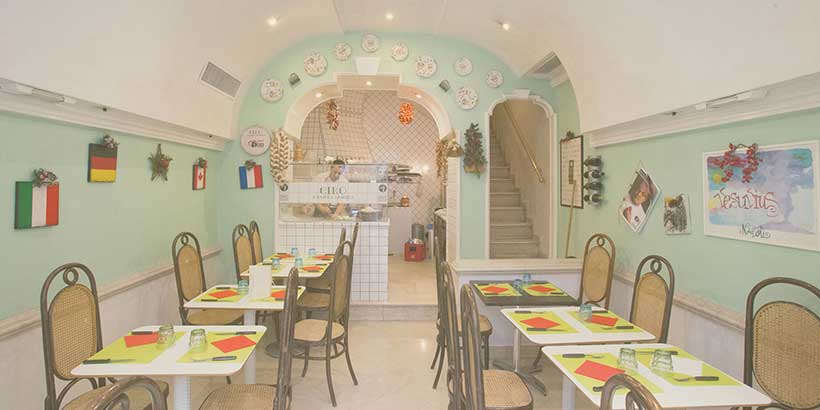 Intérieur d’un restaurant à Naples avec tables dressées, ambiance conviviale et cuisine ouverte en arrière-plan.