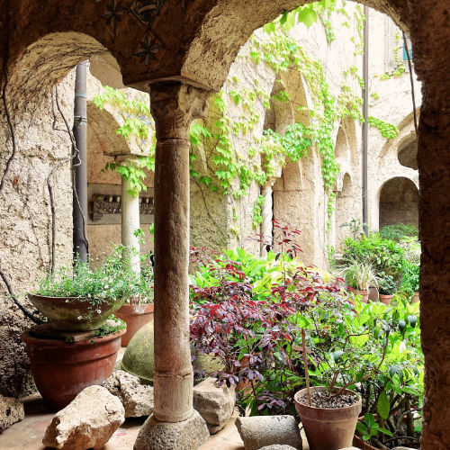 Arcades arabo-normandes et végétation luxuriante dans le cloître historique de la Villa Rufolo à Ravello.