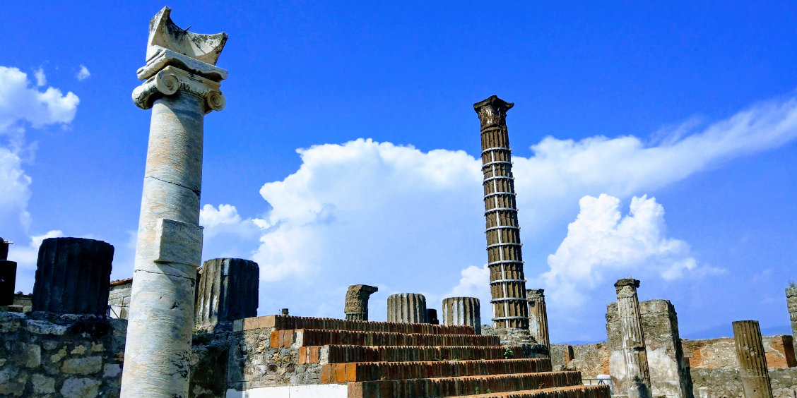 Colonne ionique blanche et colonnes en ruines sur le site du temple d'Apollon à Pompéi sous un ciel bleu parsemé de nuages.