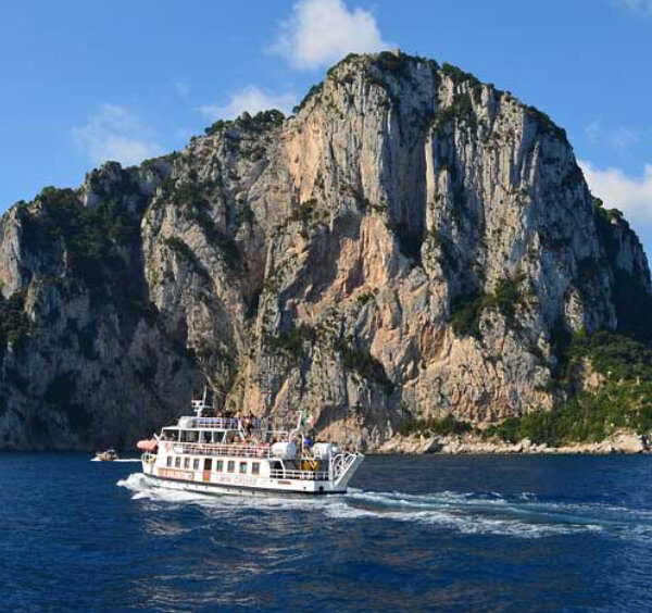 Bateau de touristes naviguant devant les Faraglioni de Capri sous un ciel bleu.