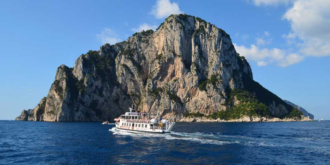 Bateau de touristes naviguant devant les Faraglioni de Capri sous un ciel bleu.